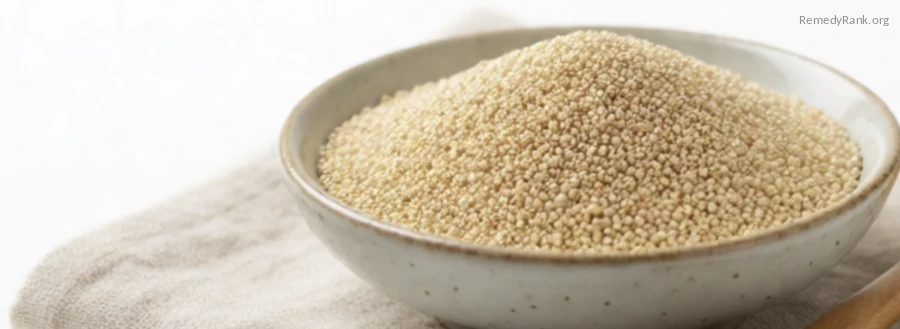 Tiny pale amaranth grains in a ceramic bowl beside a wooden spoon.